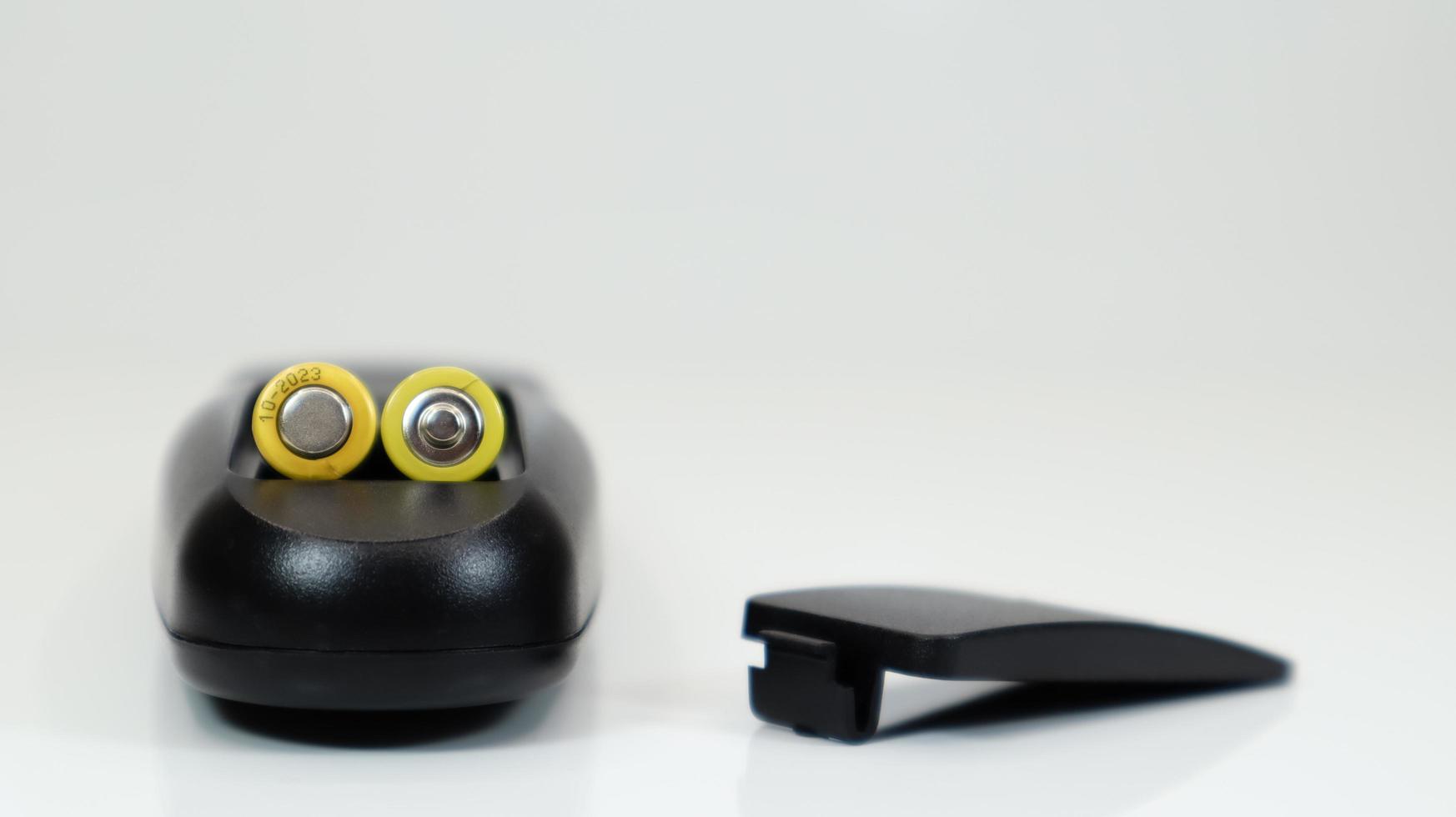 Black remote control with yellow AAA batteries on a white background. Battery replacement, spare parts. Remote control battery compartment close-up. photo