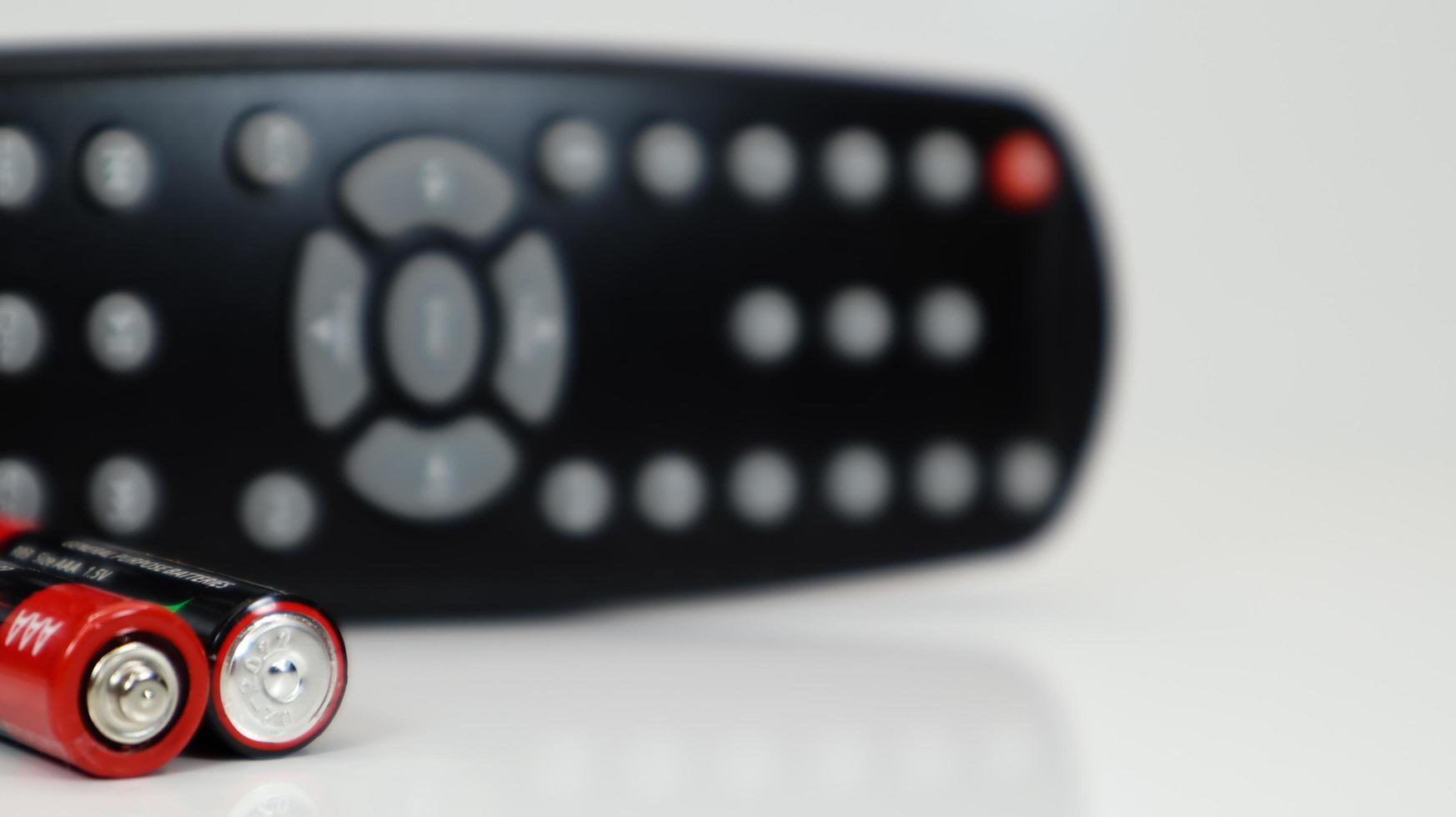 Black TV remote control with AAA alkaline batteries in red and white on a white background. Battery replacement, spare parts. Remote control battery compartment close-up. photo