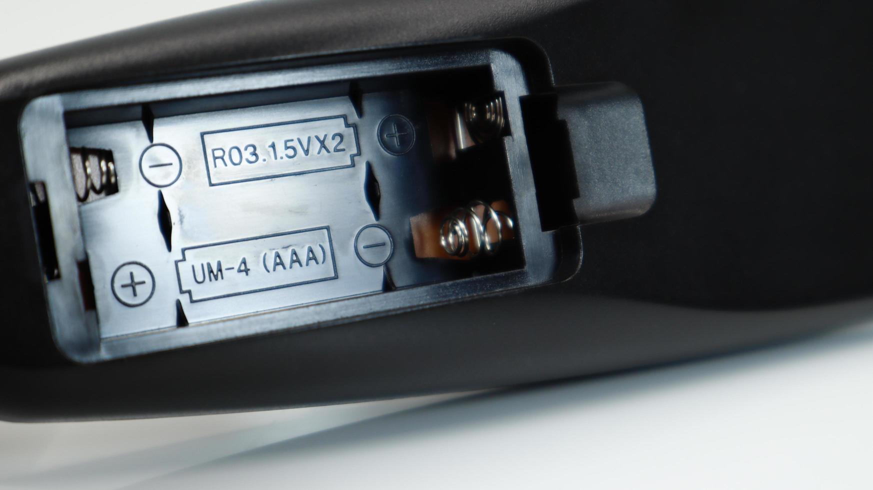 Black TV remote control with AAA alkaline batteries on a white background. Battery replacement, spare parts. Close up of an empty battery compartment of the remote control. photo