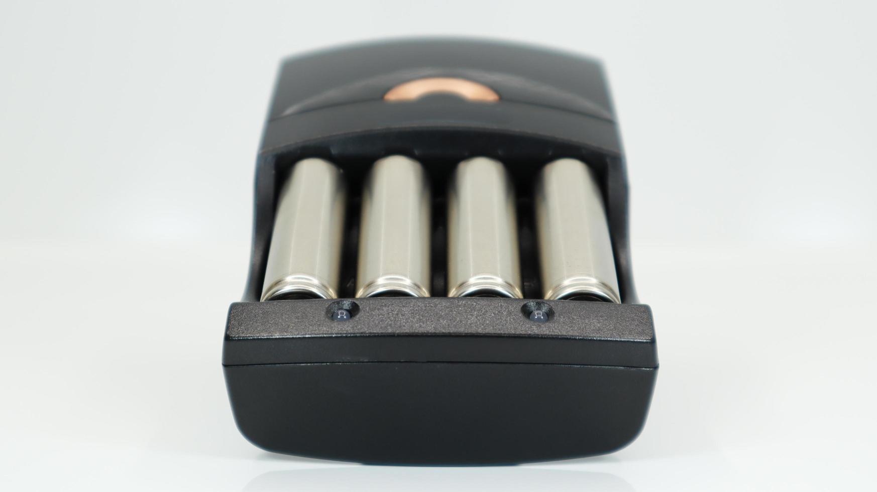 Rechargeable alkaline batteries in a battery charger on a white background. AA fast charger in black. The battery is charging. photo