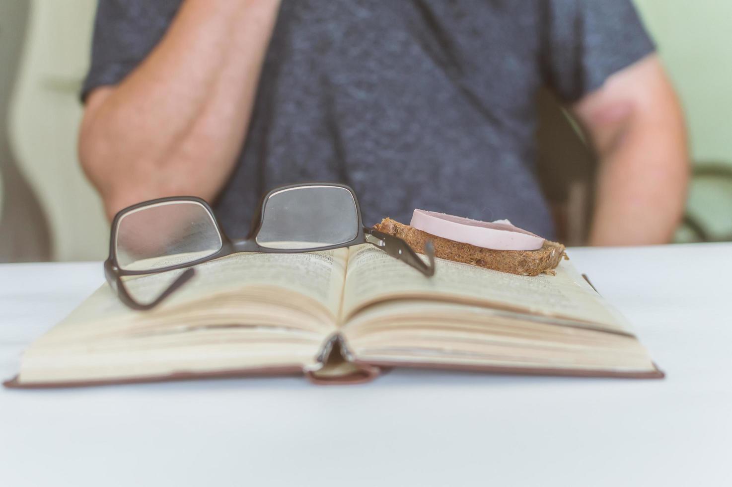 man reading a book at the table, having a snack while reading, a short break photo