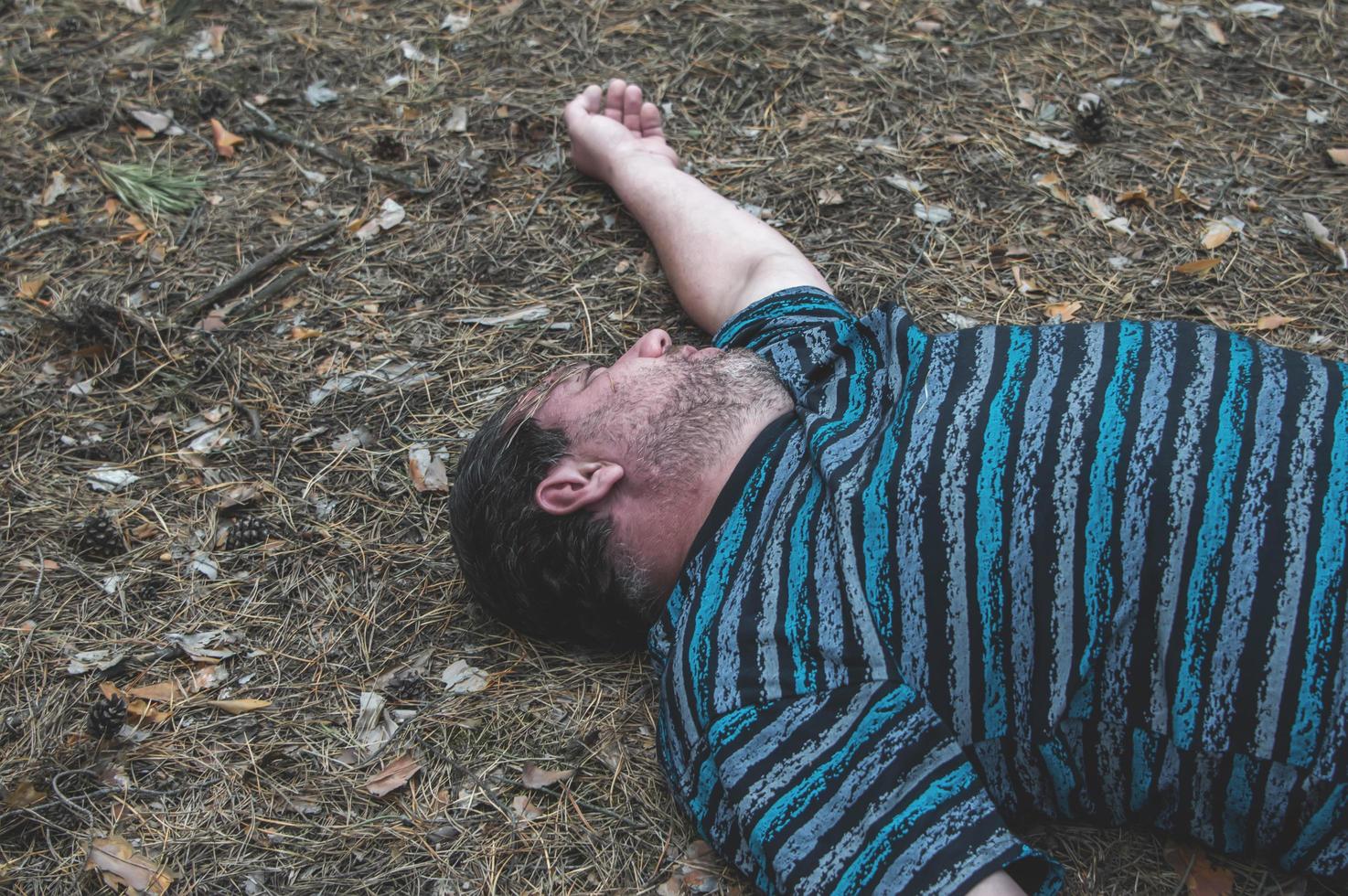 Murder in the woods. The body of a man in a blue t-shirt lies on the ground among the trees in the forest. Victim of an attack. photo