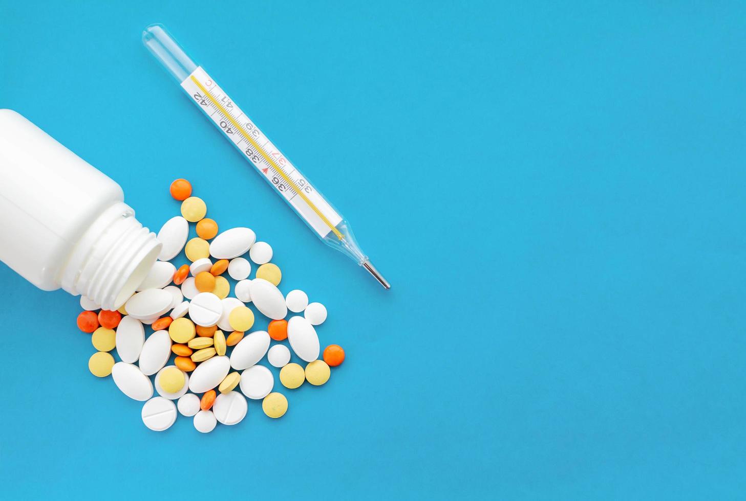 A jar of pills and a thermometer on a blue background. Concept of health protection. photo