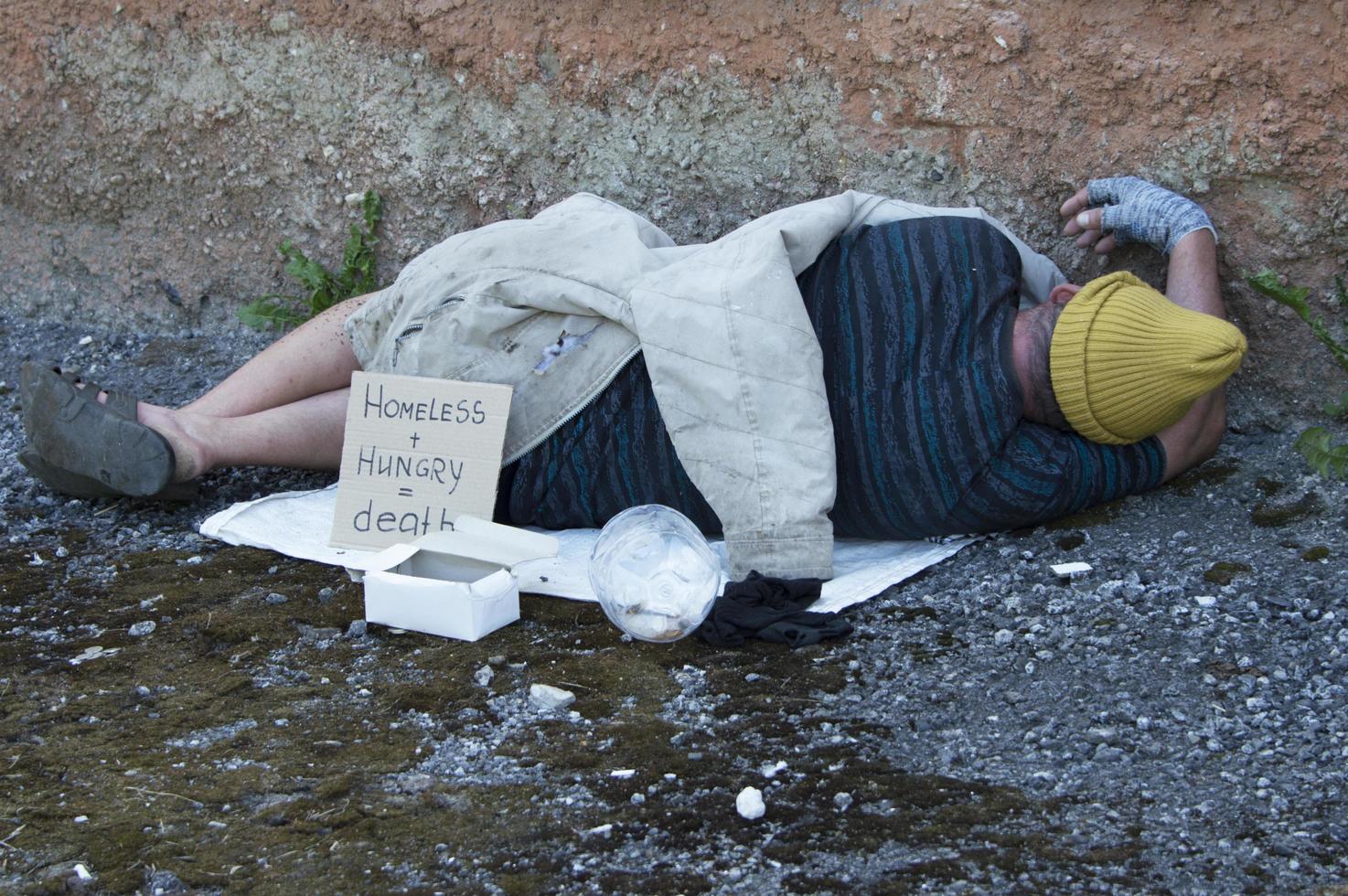 Un vagabundo está tirado en la calle con un letrero que dice necesito una casa. Pobreza, miseria, desempleo. foto