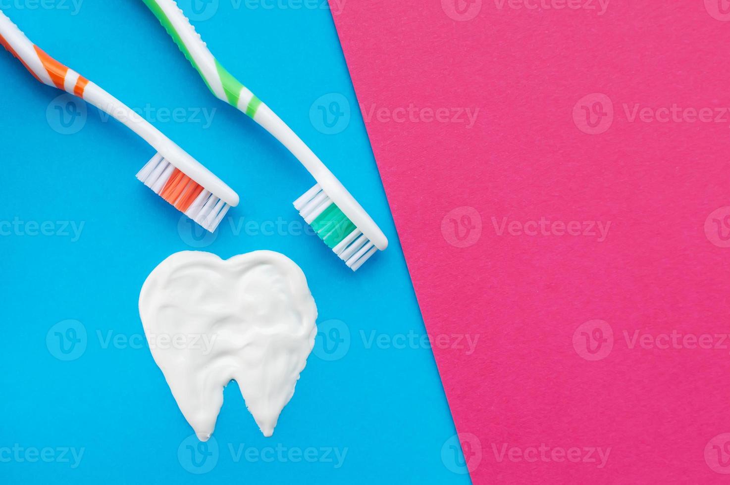Multi-colored toothbrushes on a blue and pink background with a tooth pattern drawn with toothpaste. The view from the top. photo