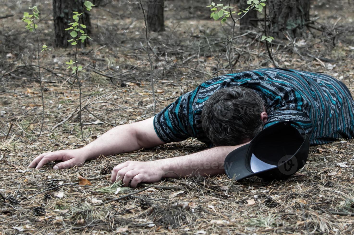 Murder in the woods. The body of a man in a blue t-shirt and trousers lies on the ground among the trees in the forest. Victim of an attack. photo