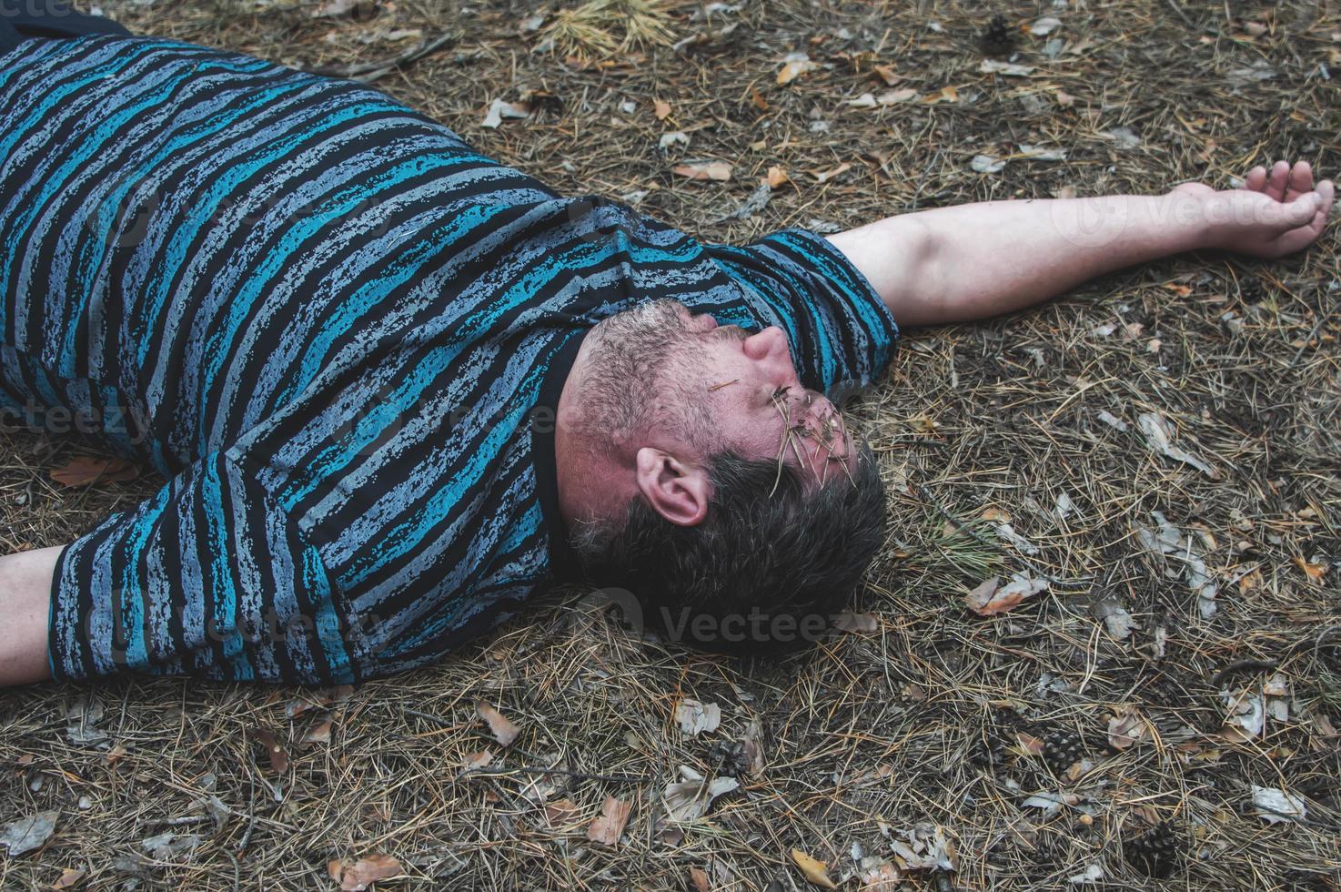 Murder in the woods. The body of a man in a blue t-shirt lies on the ground among the trees in the forest. Victim of an attack. photo