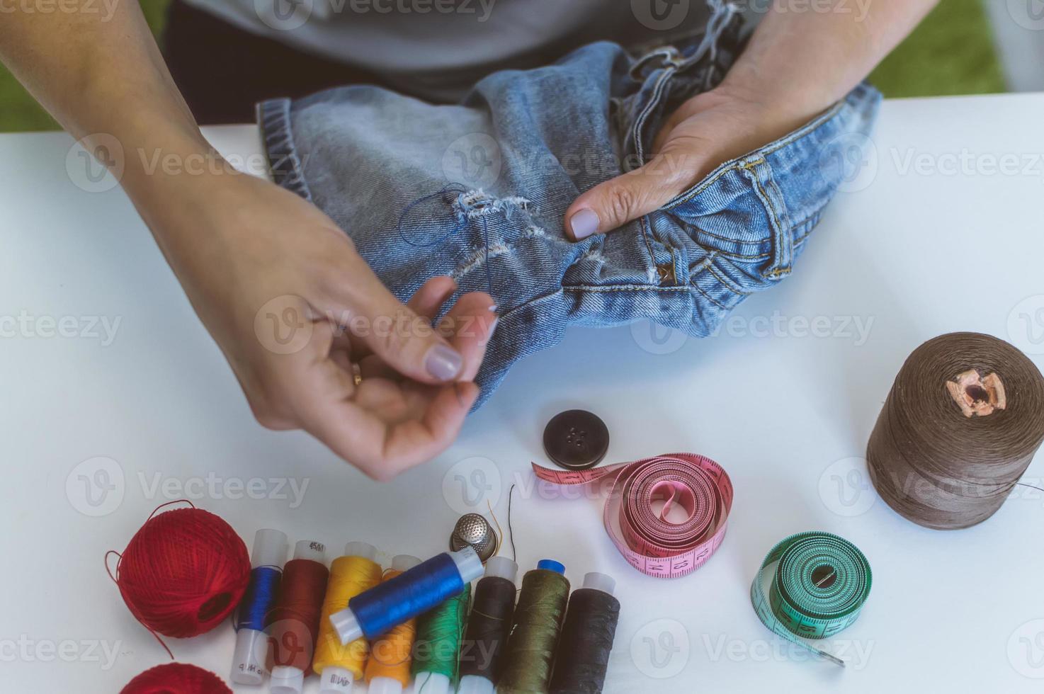 women's hands, a tailor sews clothes at a table on which spools of thread lie photo