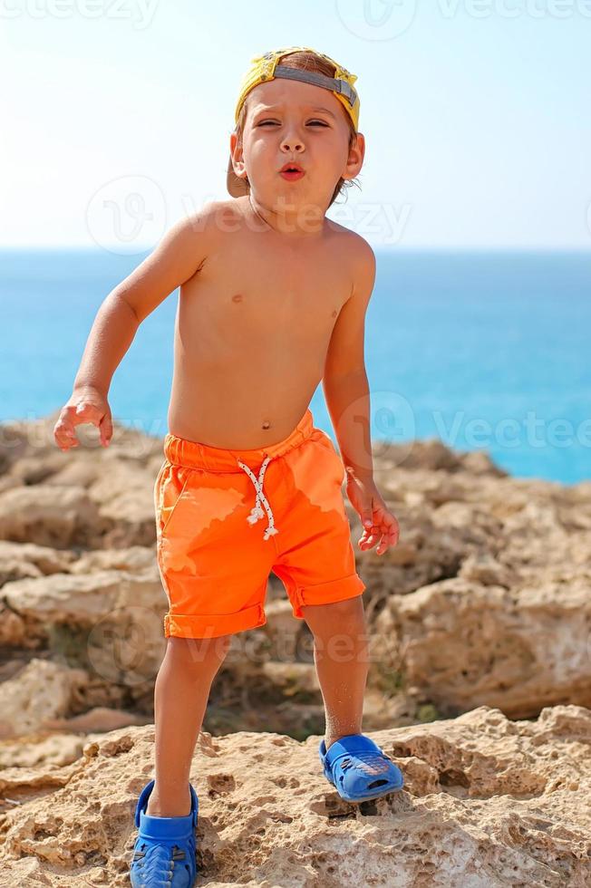 un niño en pantalones cortos y una gorra en la playa en un día soleado. turismo, viajes, vacaciones en familia. foto