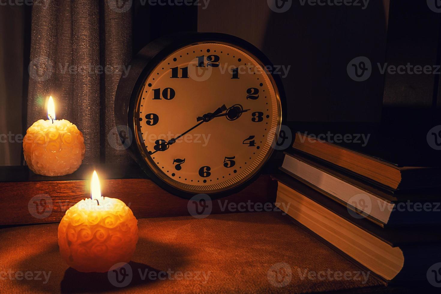 libros sobre la mesa con un reloj iluminado por luces nocturnas y velas foto