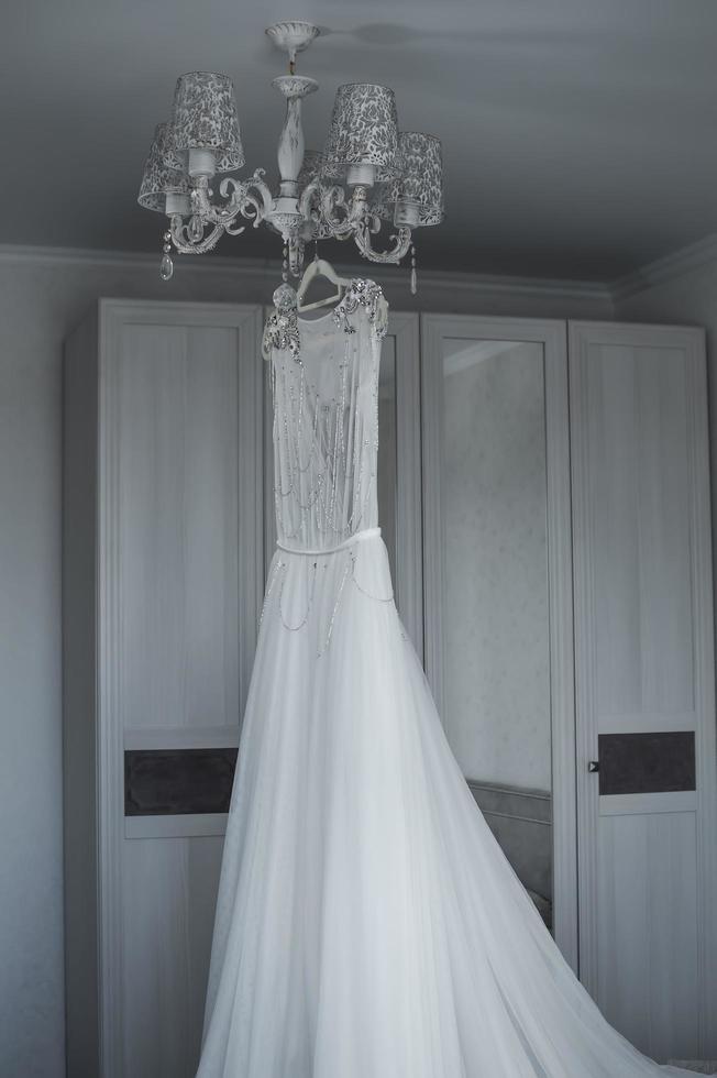 the bride's wedding dress hangs on the chandelier. wedding. selective focus. film grain. photo