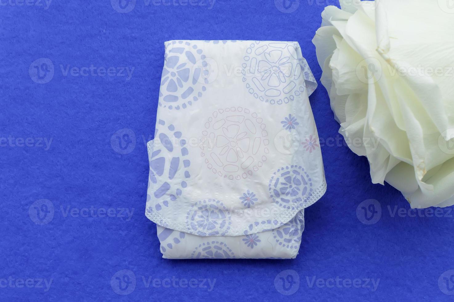 Women's sanitary napkin and white rose on a lilac background. Concept of women's health and hygiene. photo