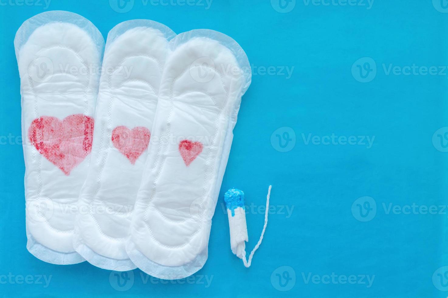 Women's pads with red hearts of different sizes and a tampon on a blue background. The concept of the menstrual cycle. photo