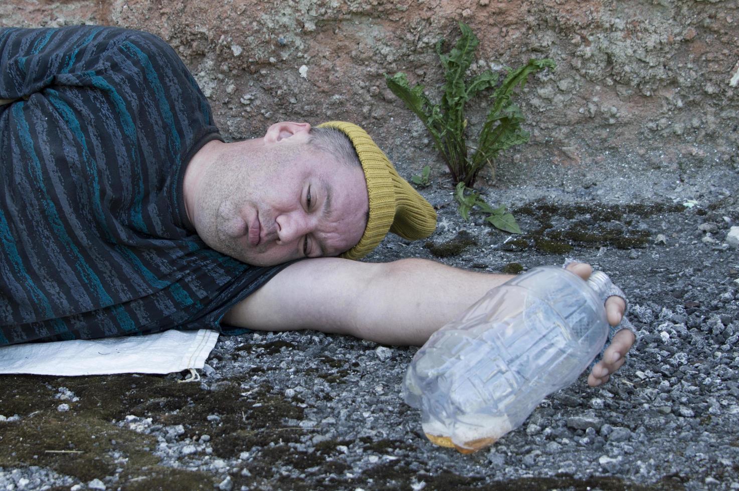 A homeless man who is intoxicated is sleeping on the street holding a beer bottle in his hands. Poverty, unemployment, alcoholism. photo