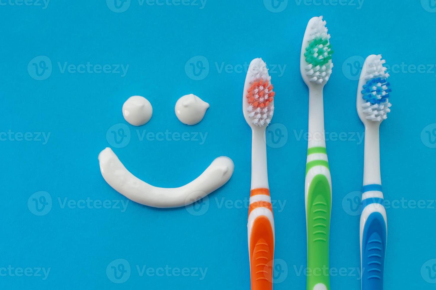 Multicolored toothbrushes on a blue background with a smile painted with toothpaste. The view from the top. photo