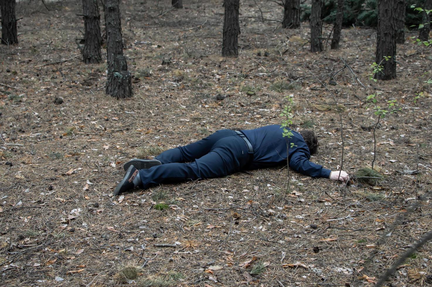 asesinato en el bosque. el cuerpo de un hombre con camisa y pantalón azul yace en el suelo entre los árboles del bosque. víctima de un ataque. foto