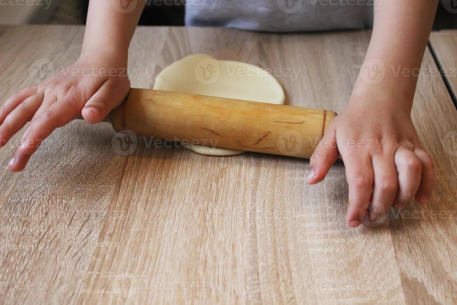 The child's hands roll out the tight dough for dumplings on the table with a rolling pin. Home cooking. Selective focus. photo