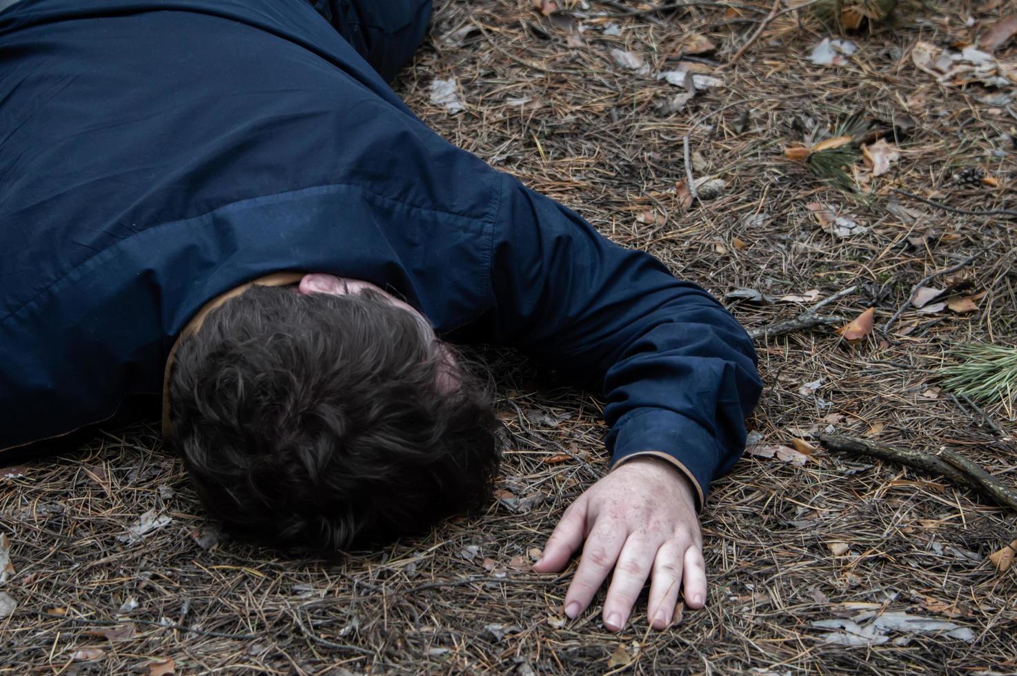 Murder in the woods. The body of a man in a blue shirt lies on the ground among the trees in the forest. Victim of an attack. photo