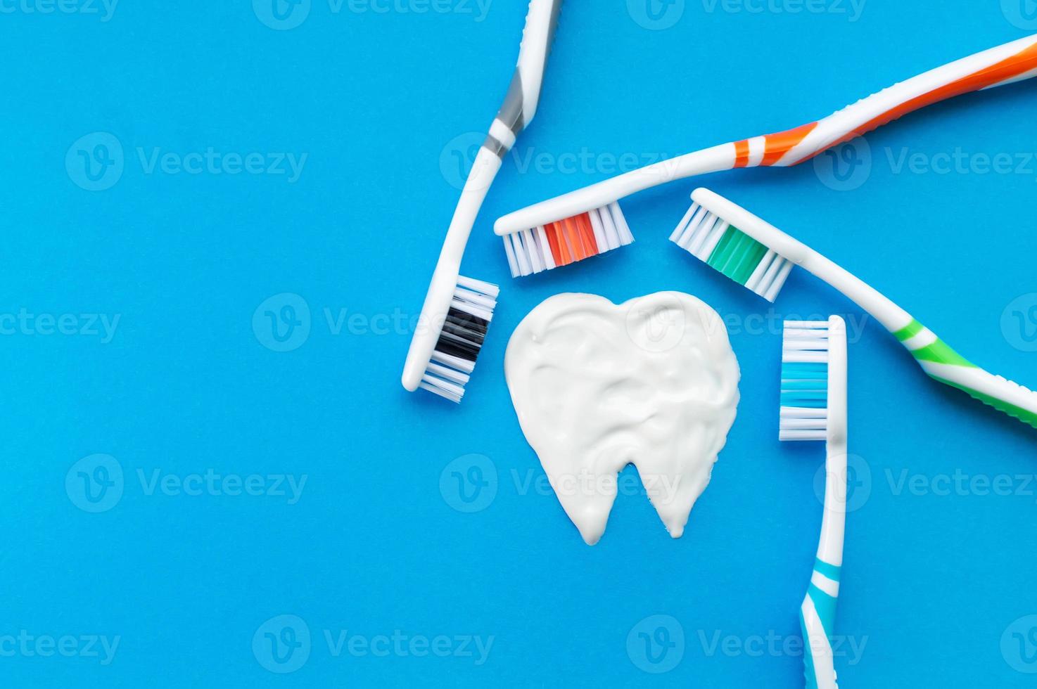 Multi-colored toothbrushes on a blue background with a tooth pattern drawn with toothpaste. The view from the top. photo