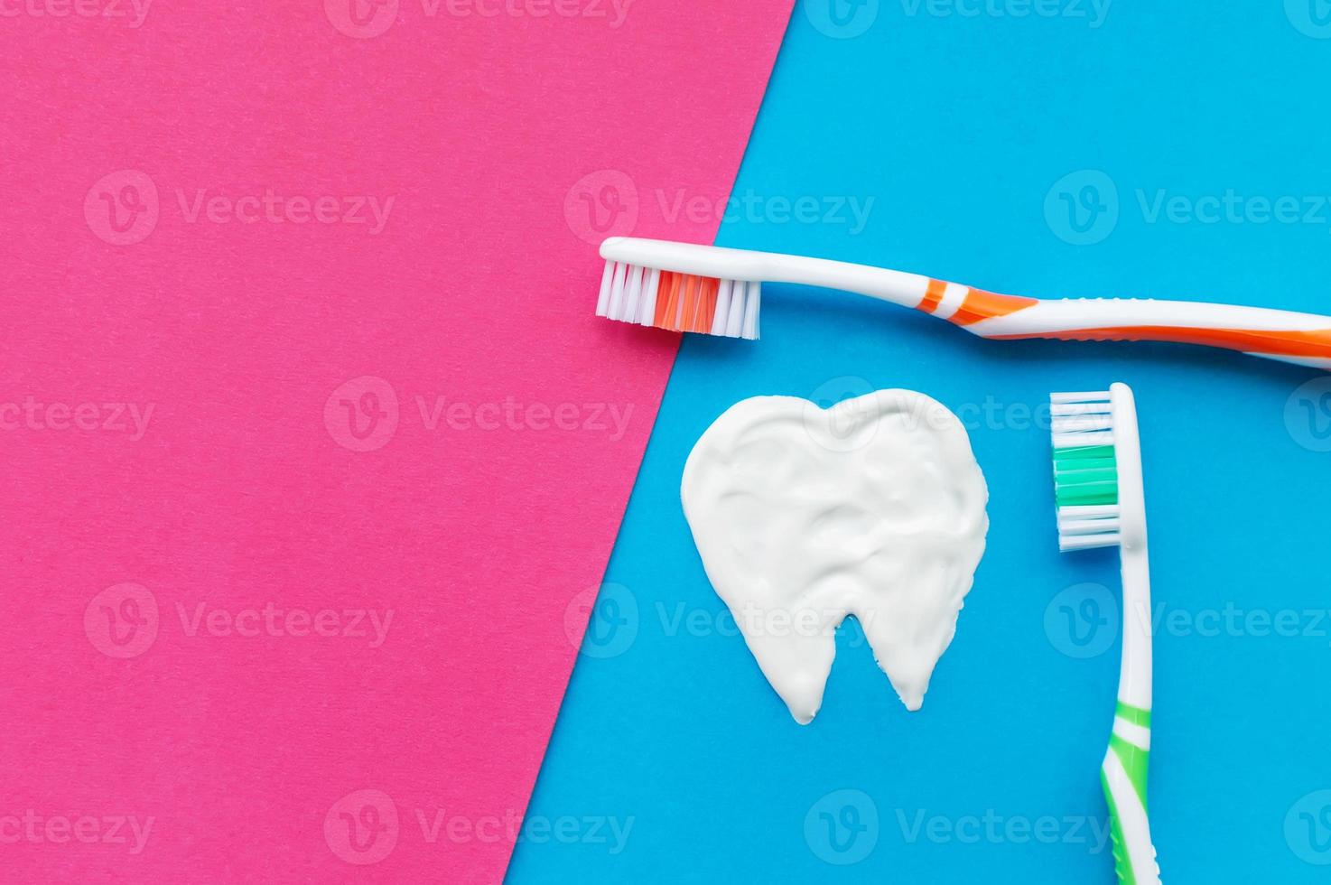 Cepillos de dientes multicolores sobre un fondo azul y rosa con un patrón de dientes dibujado con pasta de dientes. la vista desde la cima. foto