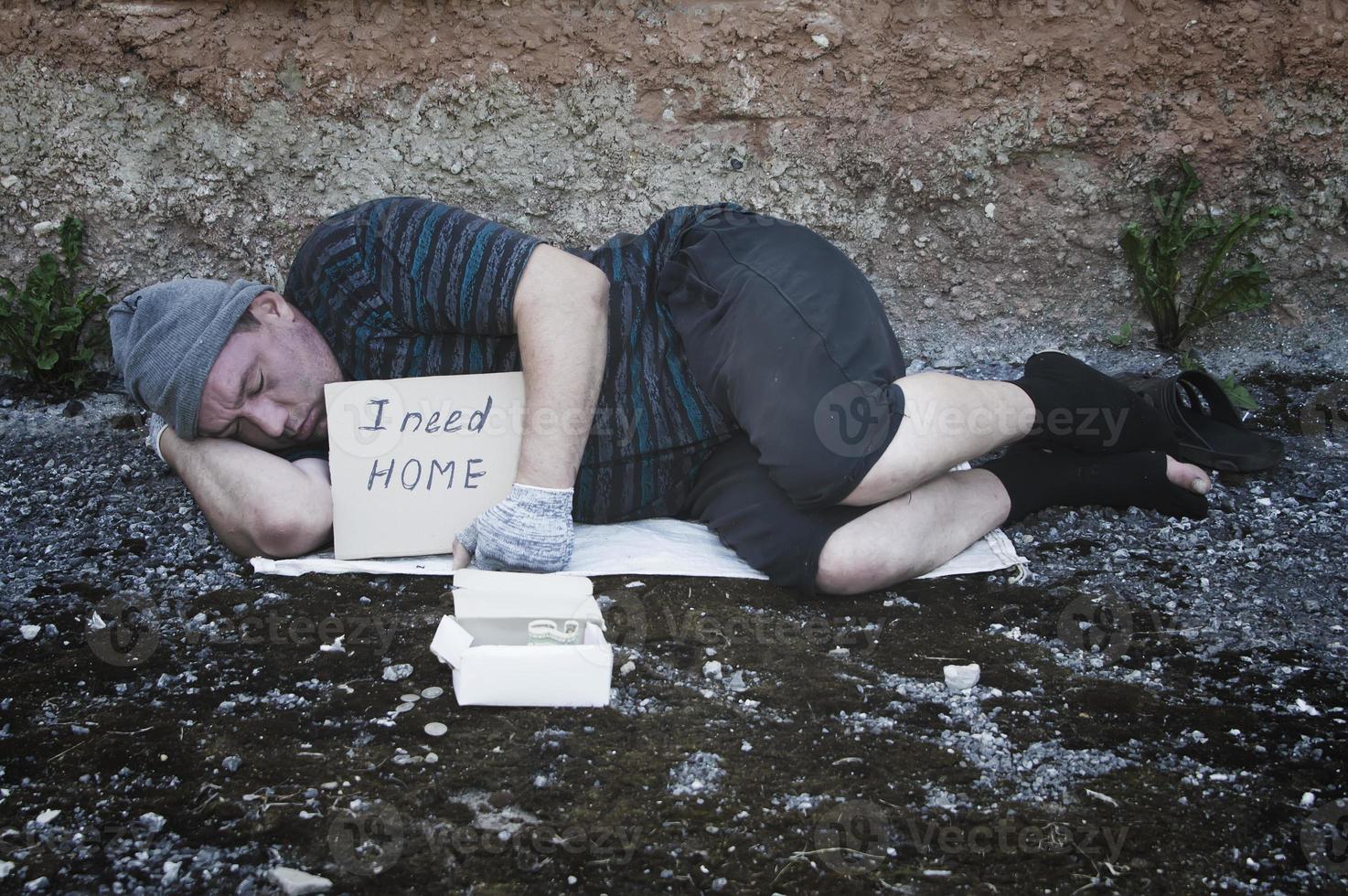 un vagabundo duerme en la calle con un letrero que dice necesito un hogar.pobreza, miseria, desempleo. foto