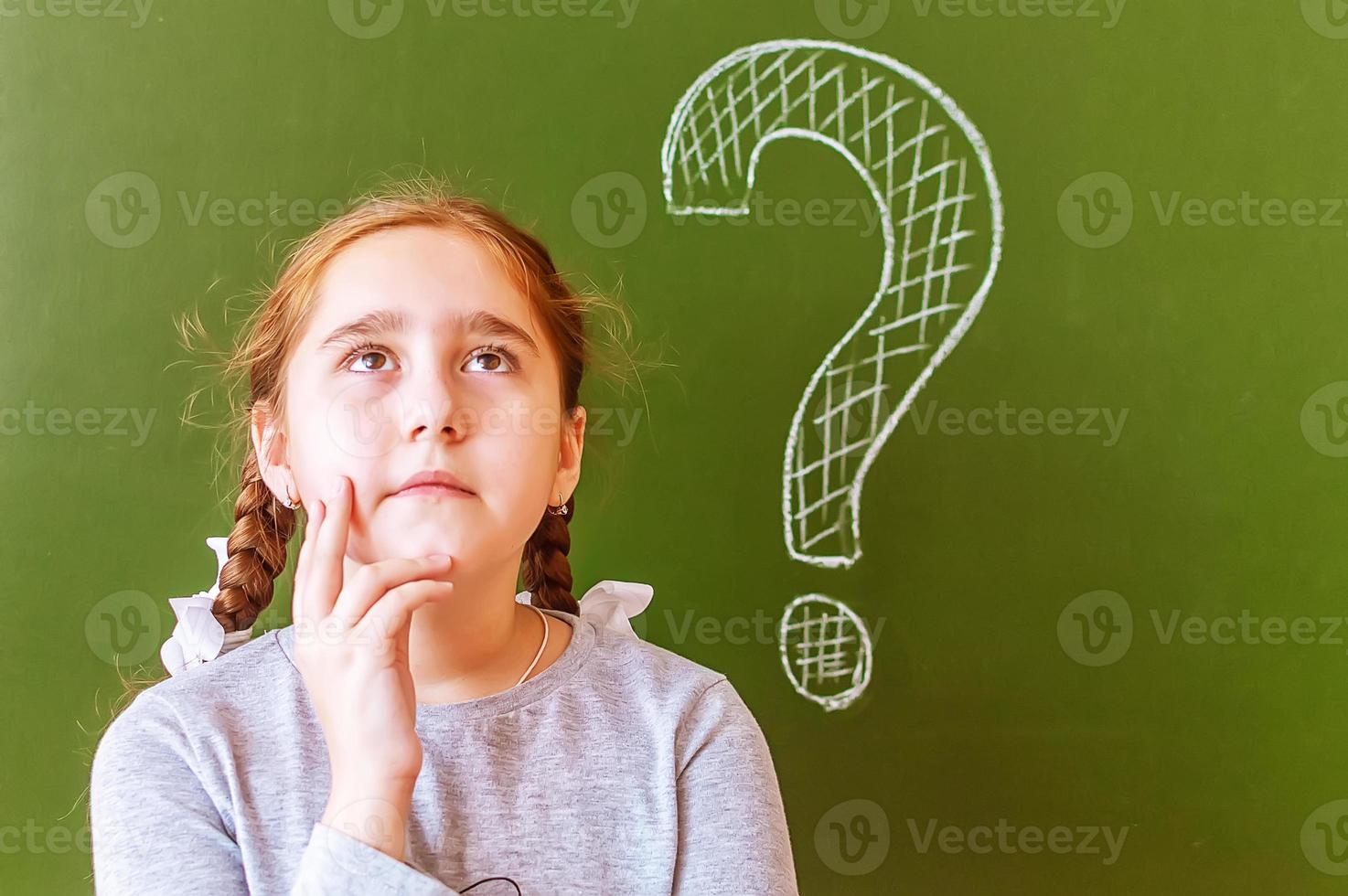 Portrait of a schoolgirl thinking about solving a problem on the blackboard during the lesson. photo