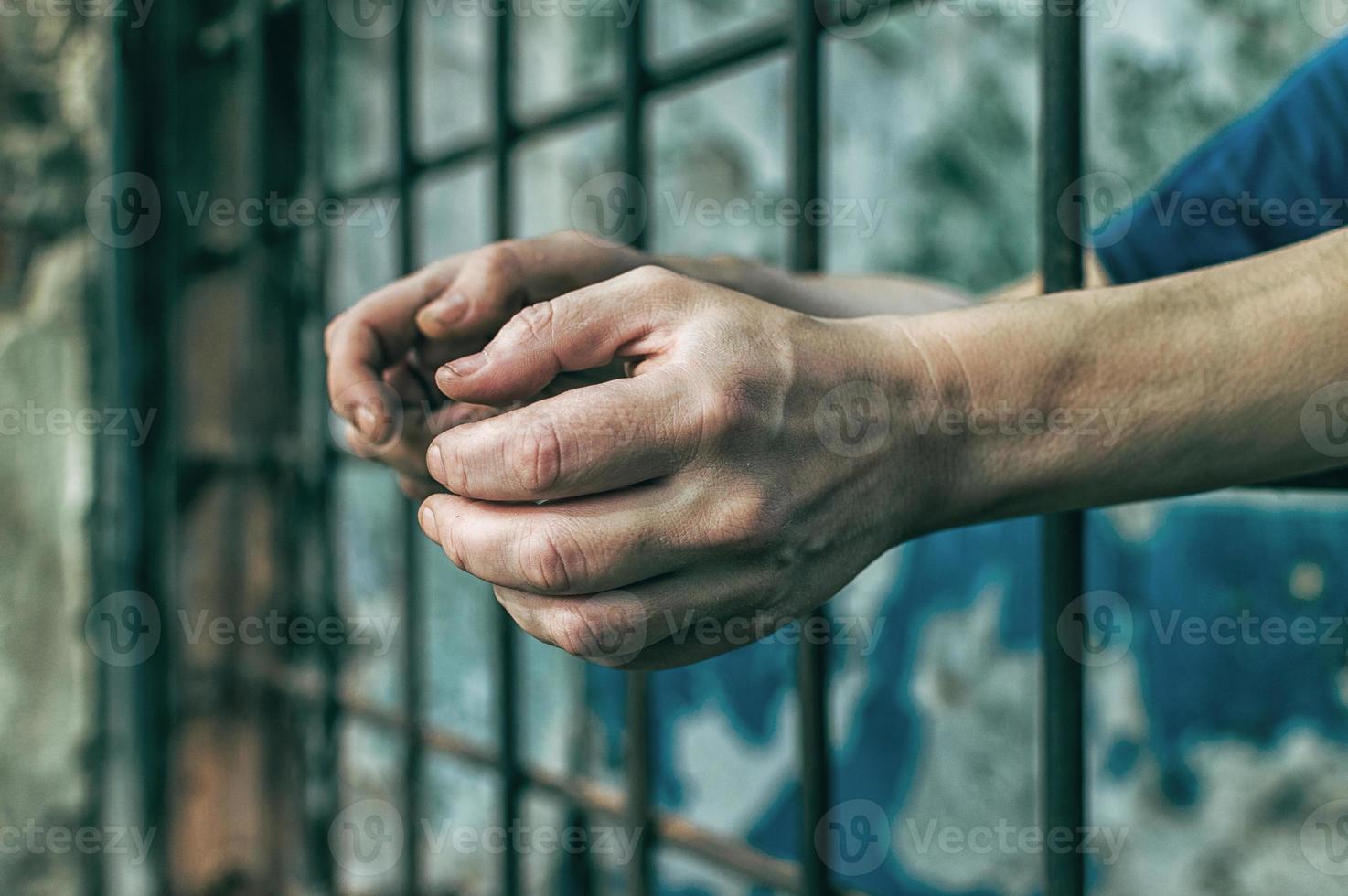 A depressed man holds his hands on the prison bars. Prisoner for the crime. Poor conditions. Scream, despair, pain, hunger. photo