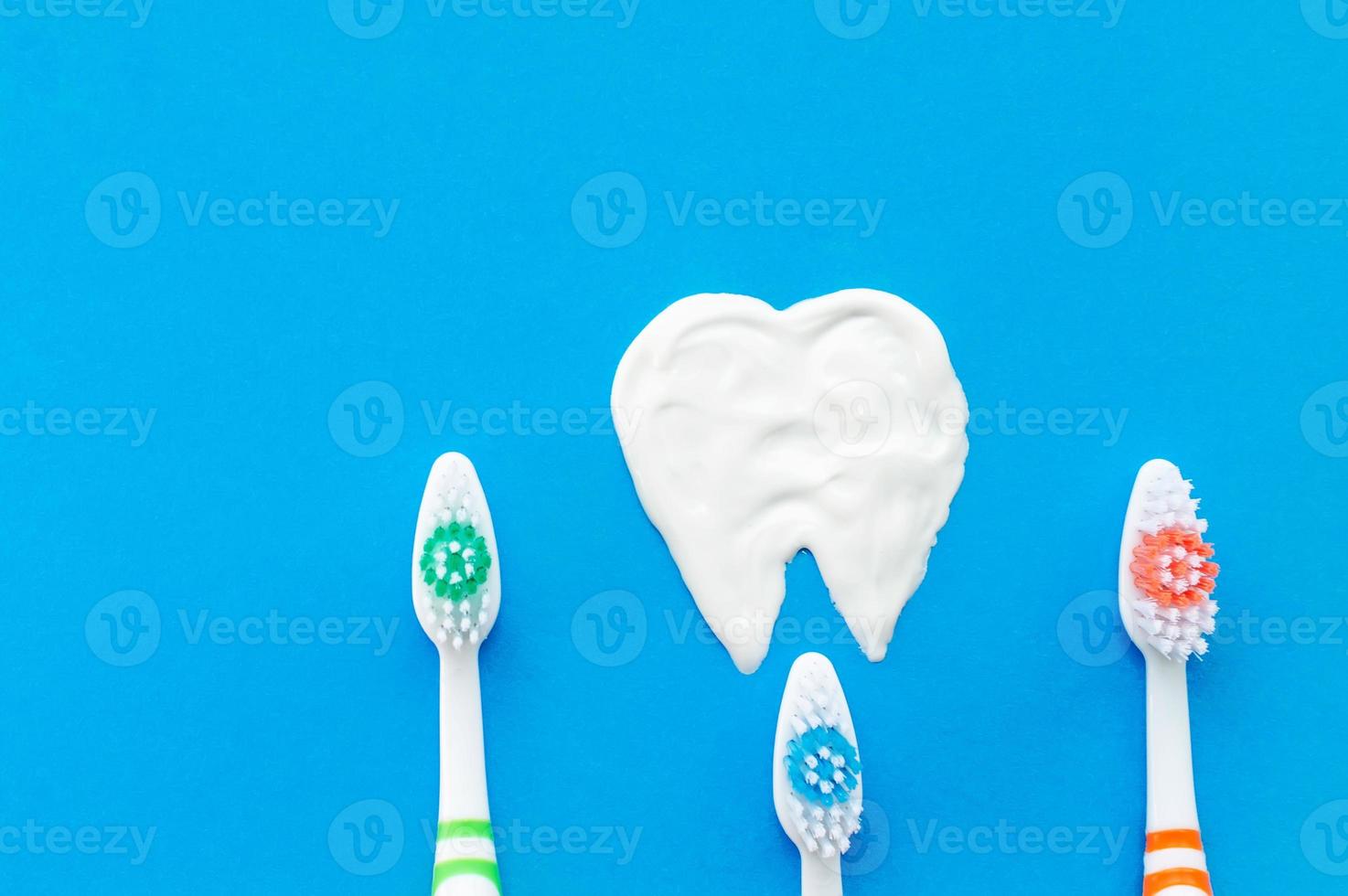 Multi-colored toothbrushes on a blue background with a tooth pattern drawn with toothpaste. The view from the top. photo