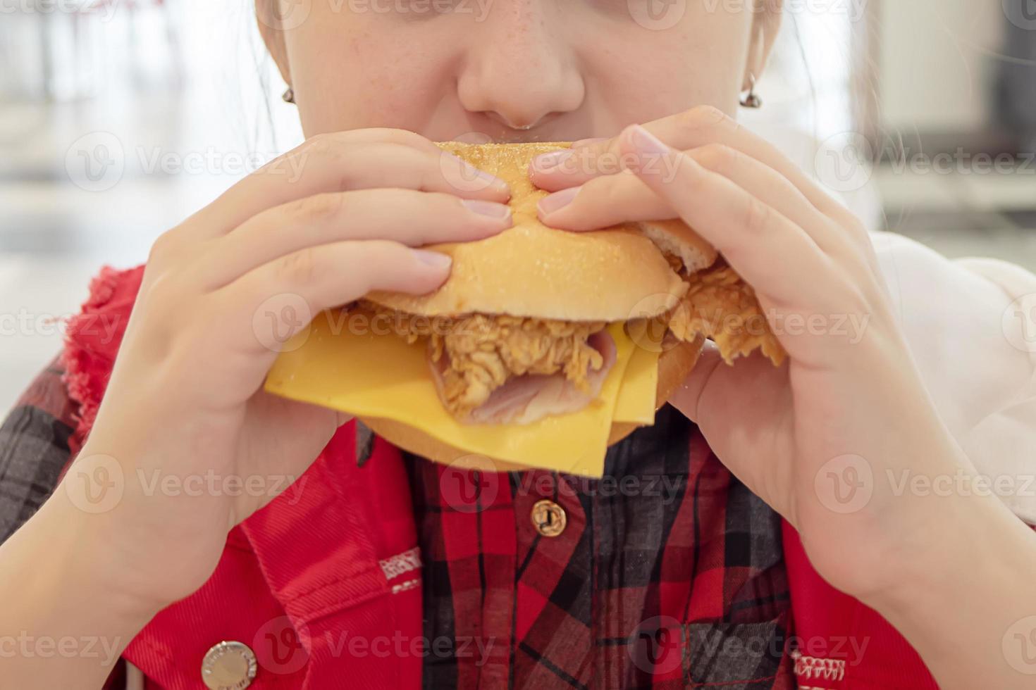 Adolescente hambrienta comiendo una hamburguesa con queso en el patio de comidas del centro comercial. comida chatarra. foto