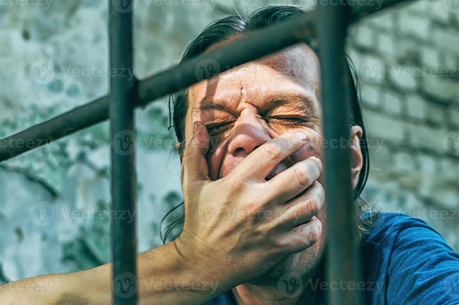 A depressed man in handcuffs behind bars. A depressed arrested male offender is jailed. Shouts, breaks, cries. photo