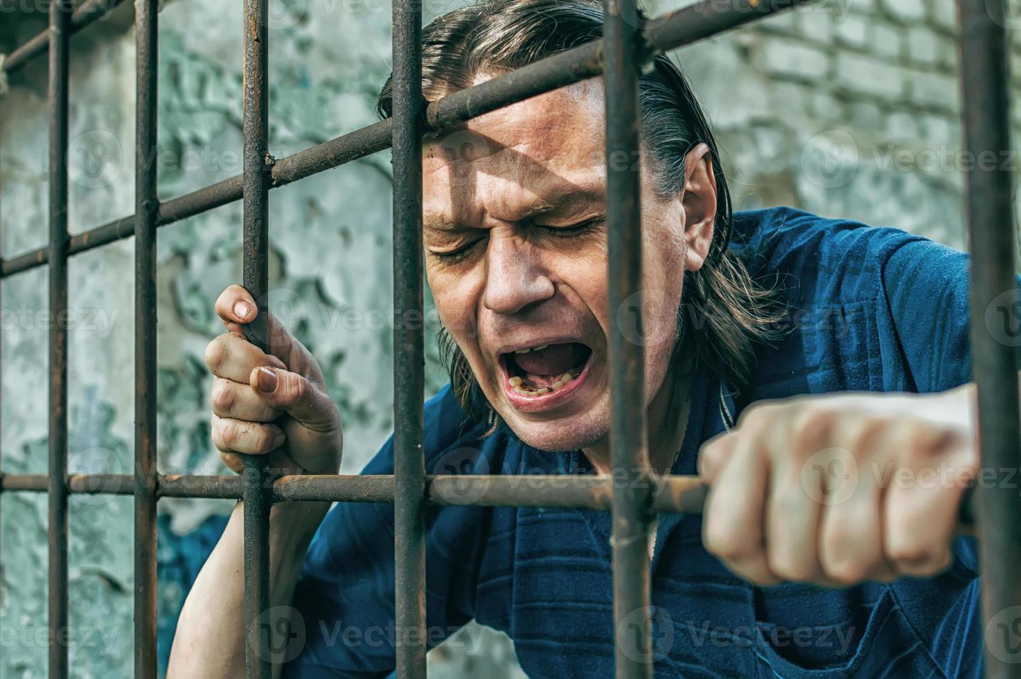 A depressed man in handcuffs behind bars. A depressed arrested male offender is jailed. Shouts, breaks, cries. photo