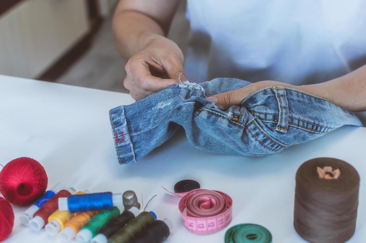 women's hands, a tailor sews clothes at a table on which spools of thread lie photo