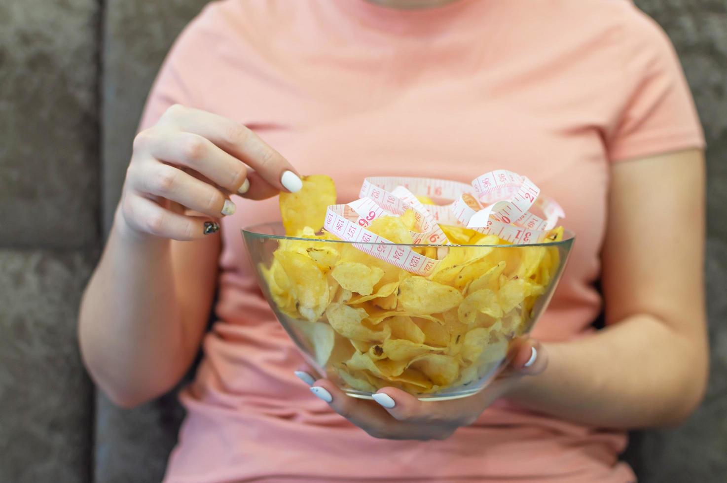 A plate of potato chips and a centimeter tape in the girl's hands. Junk food. The concept of struggle against excess weight. Selective focus, film grain. photo