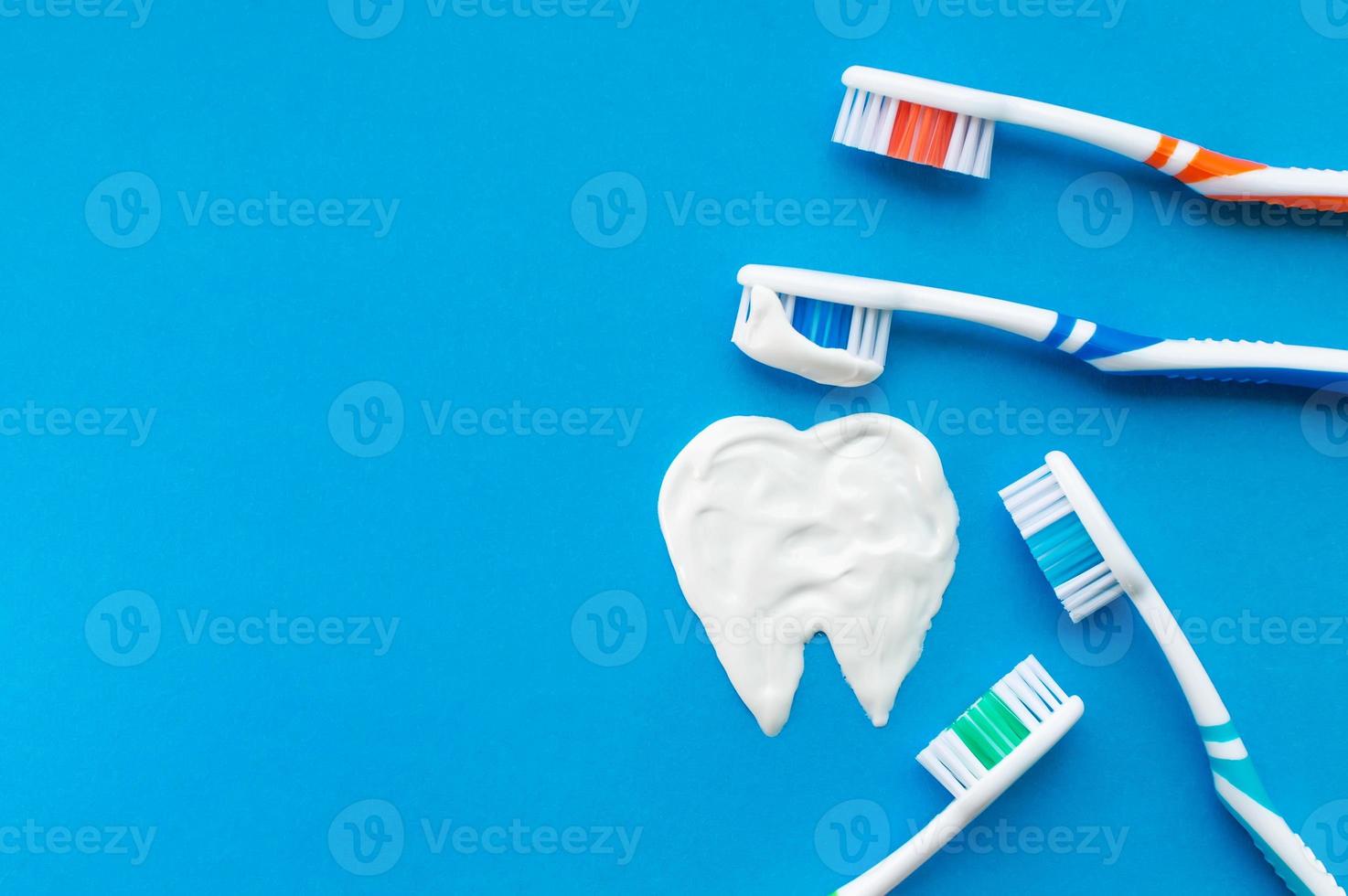 Multi-colored toothbrushes on a blue background with a tooth pattern drawn with toothpaste. The view from the top. photo