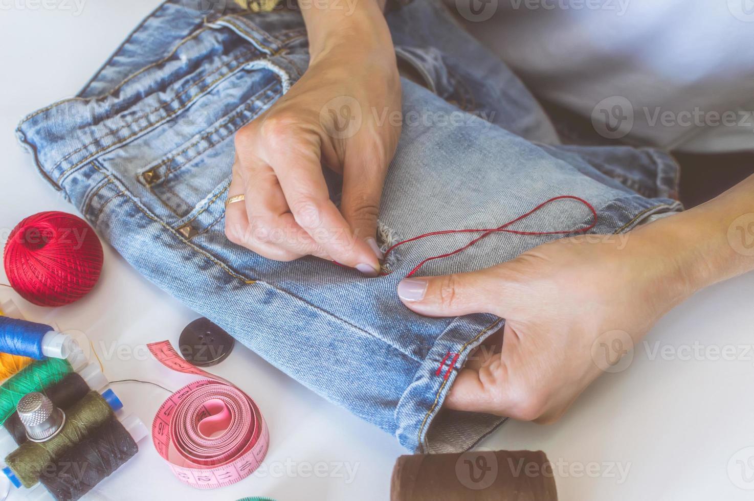 women's hands, a tailor sews clothes at a table on which spools of thread lie photo