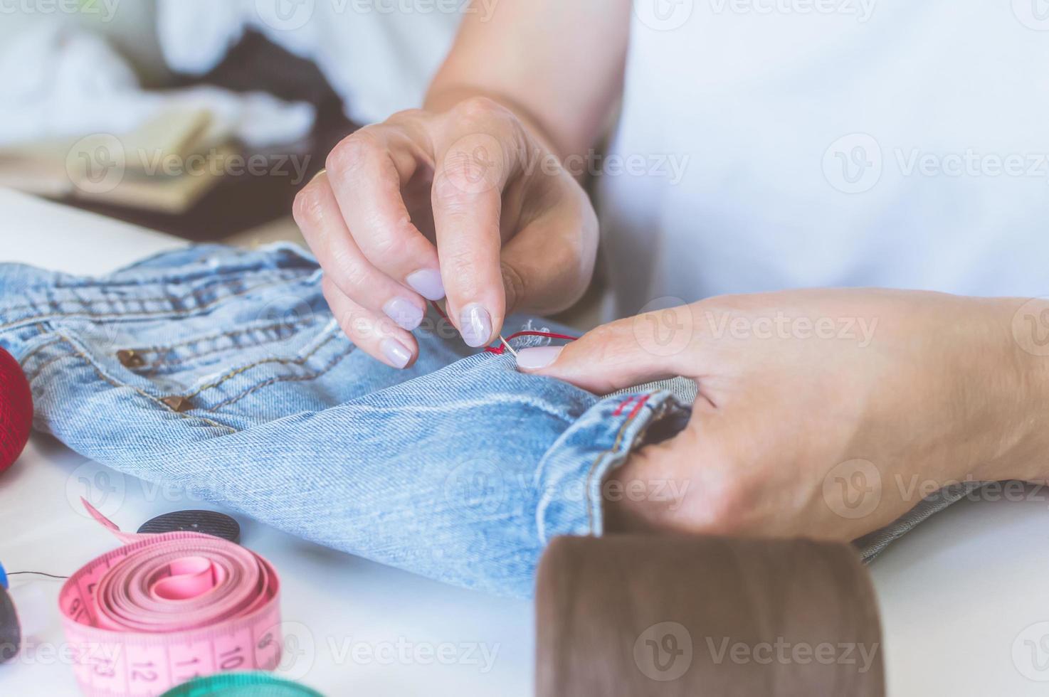 manos de mujer, un sastre cose ropa en una mesa en la que se encuentran carretes de hilo foto