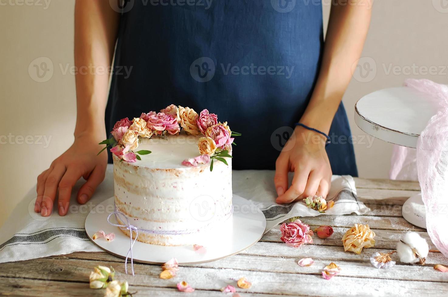 Las manos de las mujeres decoran el pastel de crema con flores frescas. foto horizontal.