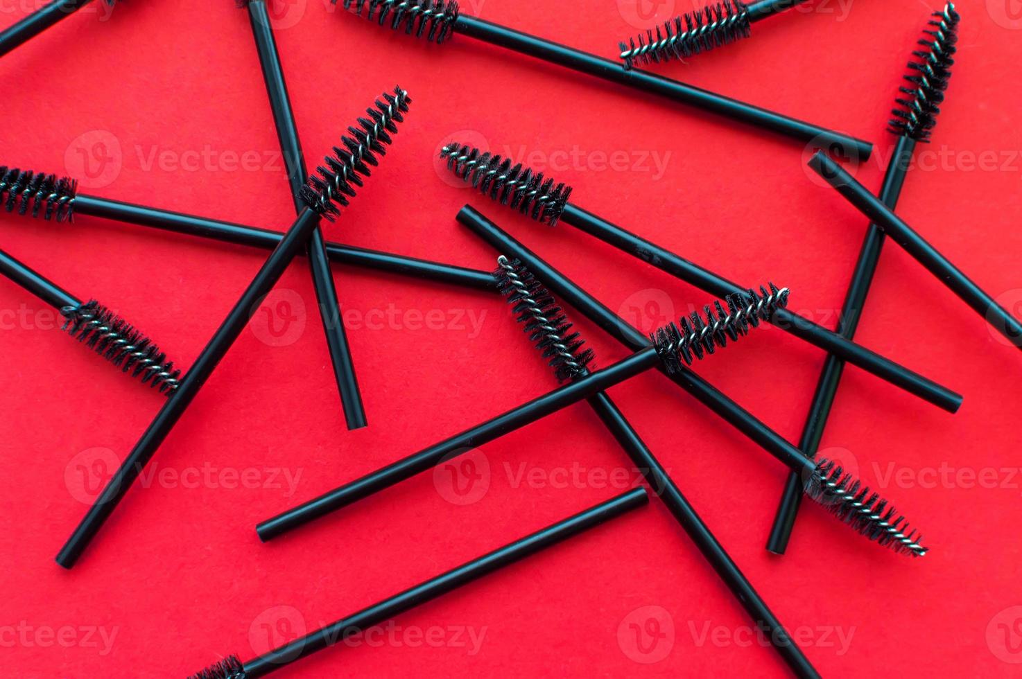 Texture. Black brushes for combing eyelashes and eyebrows scattered on a red background photo
