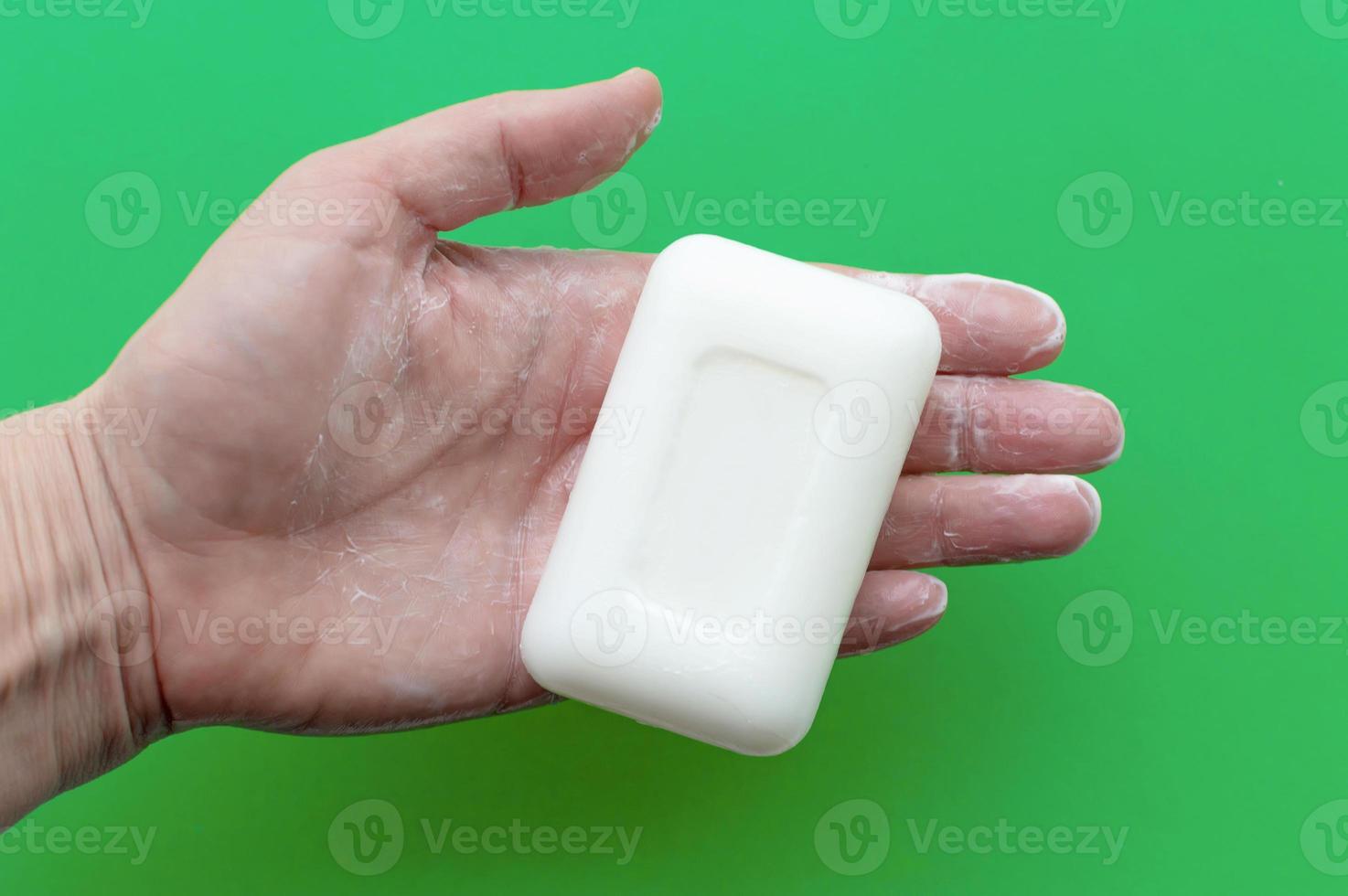 White soap in a man's hand on a green background. Concept of hygiene and body care. photo