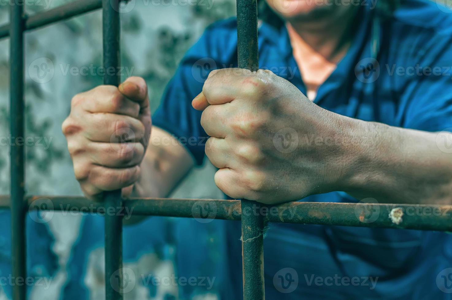 un hombre deprimido sostiene sus manos en los barrotes de la prisión. prisionero por el crimen. malas condiciones. grito, desesperación, dolor, hambre. foto