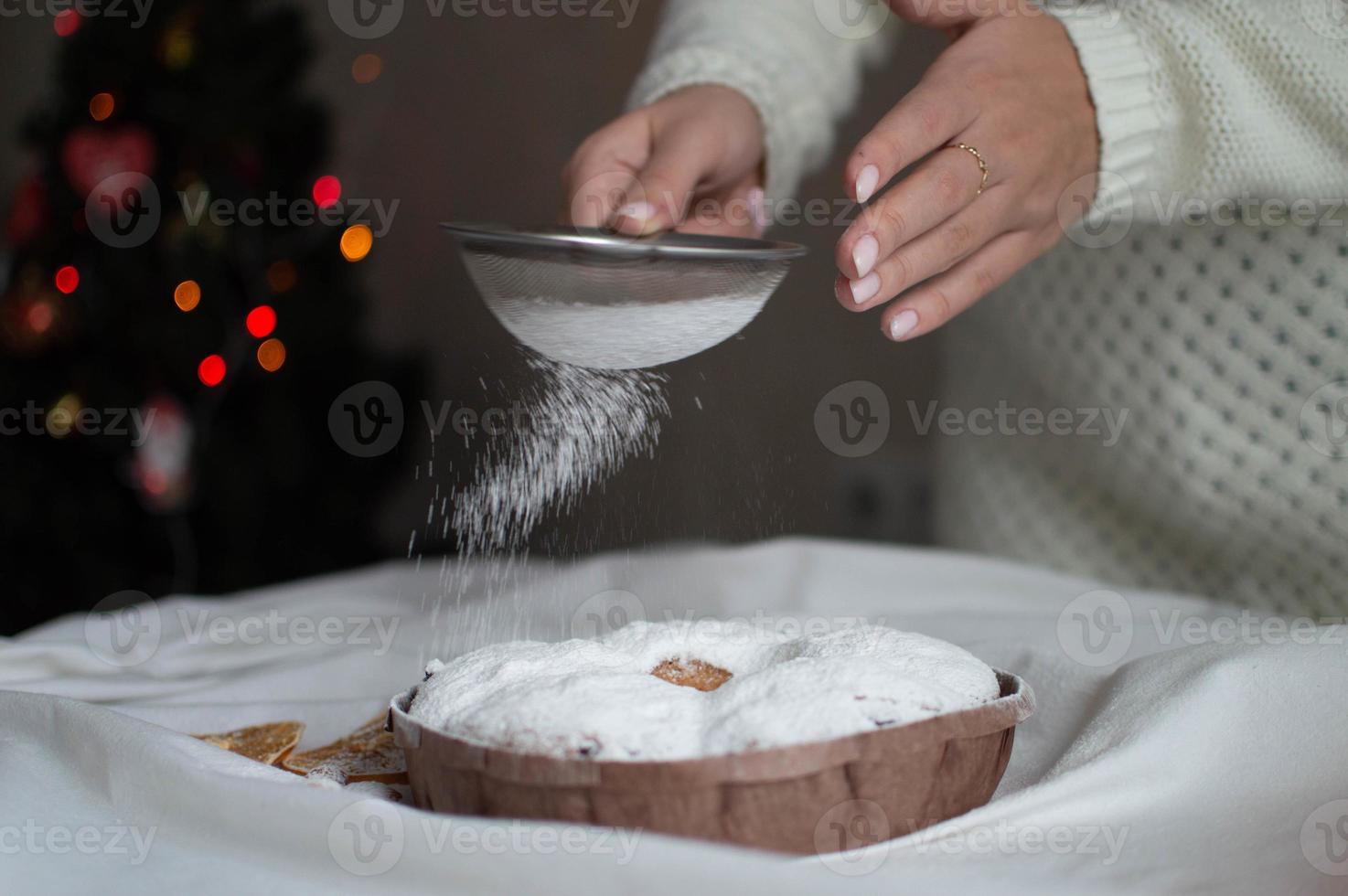 Las manos de una mujer espolvorean azúcar en polvo en un pastel de Navidad. año nuevo y navidad. de cerca. foto