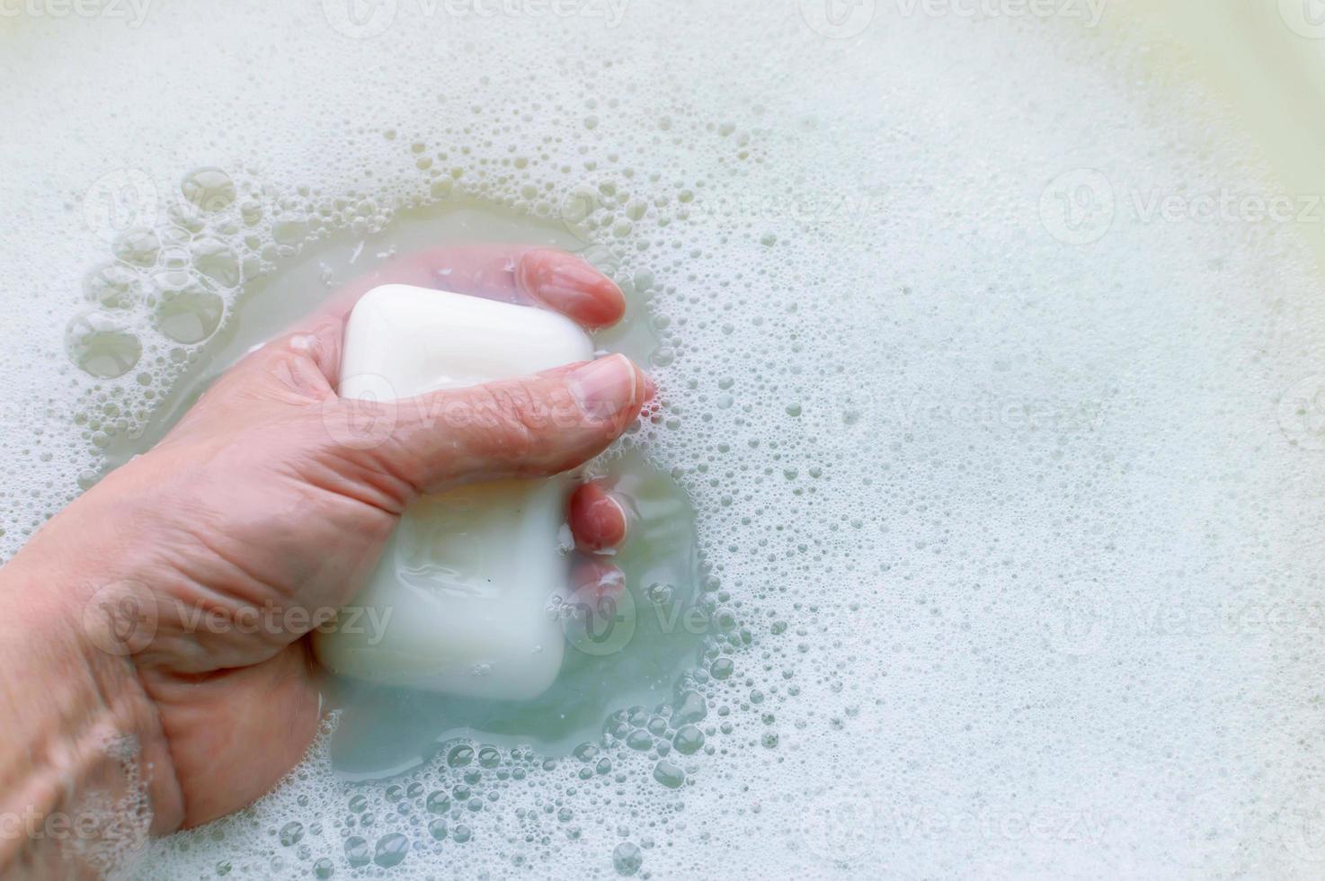 A piece of white soap in the hand of a man on a background of soap suds. Concept of hygiene and body care. photo