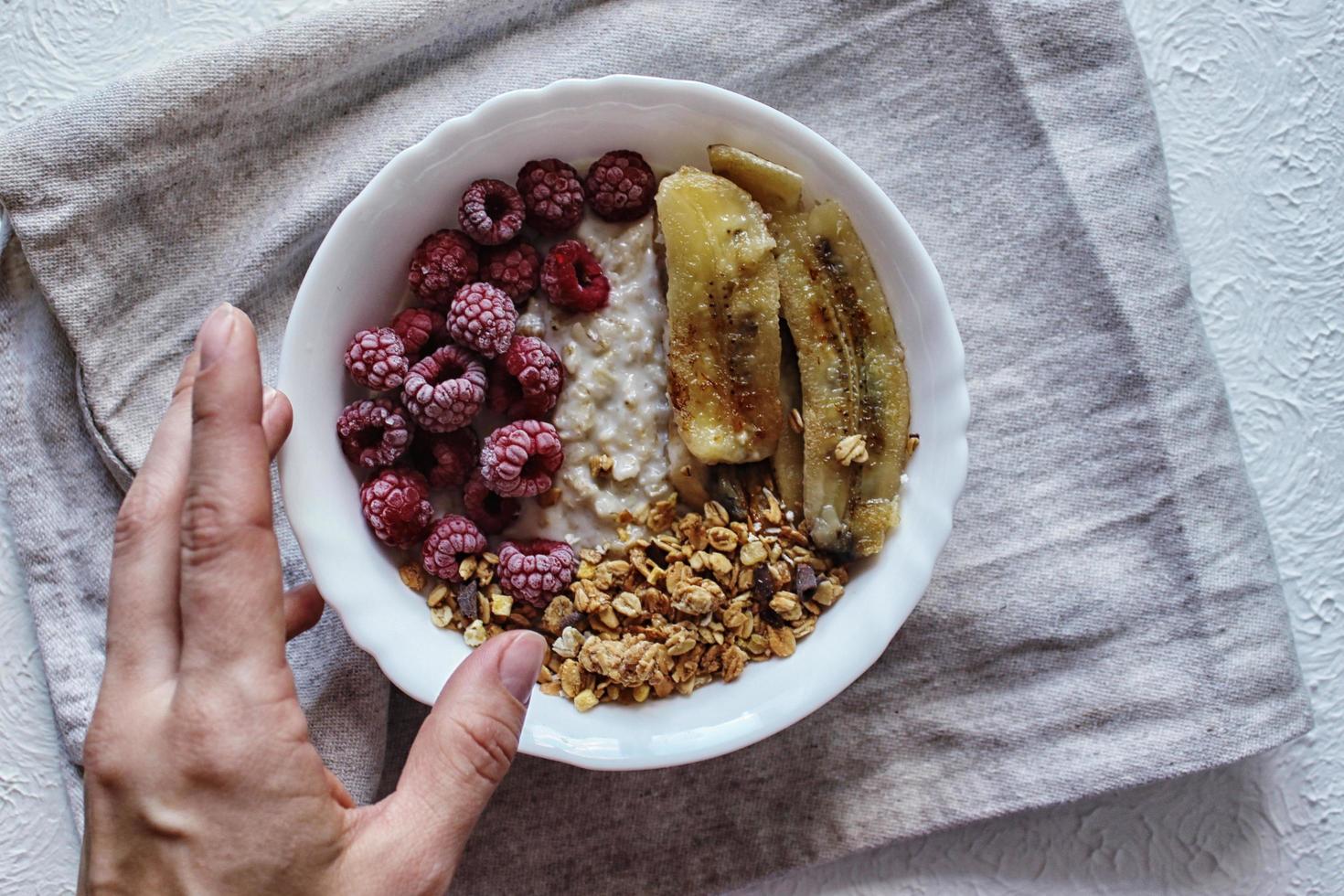 la mano de la niña sostiene un plato de gachas de avena con frambuesas y plátanos fritos. desayuno saludable. foto