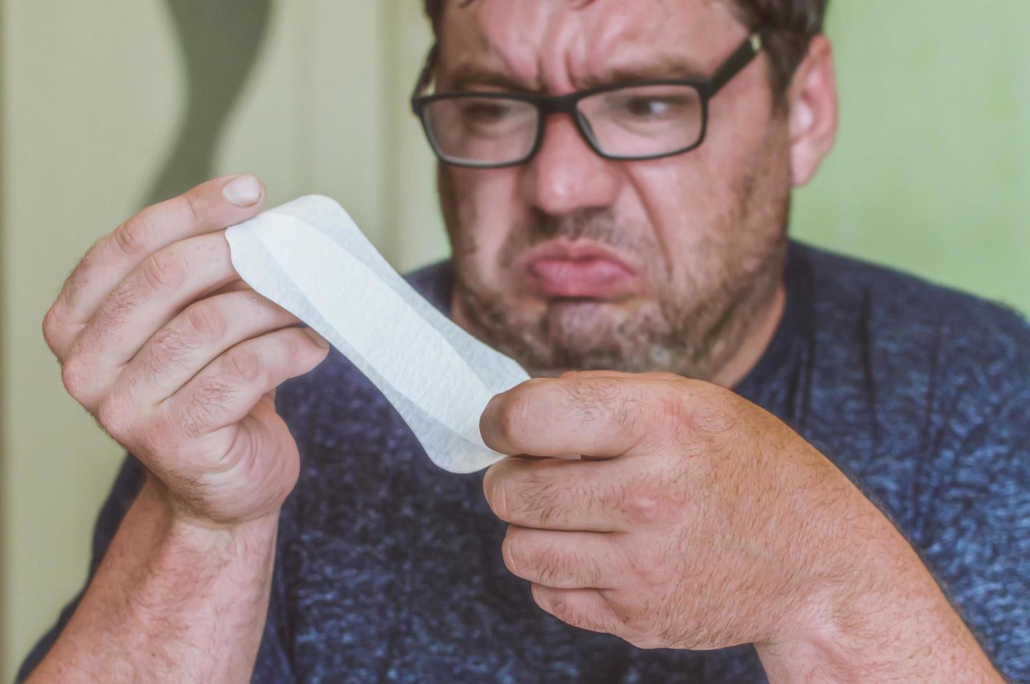 a man with glasses looks at a feminine sanitary pad with surprise photo