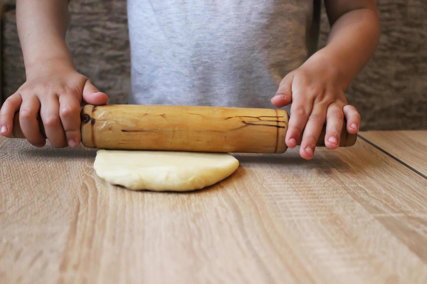 The child's hands roll out the tight dough for dumplings on the table with a rolling pin. Home cooking. Selective focus. photo