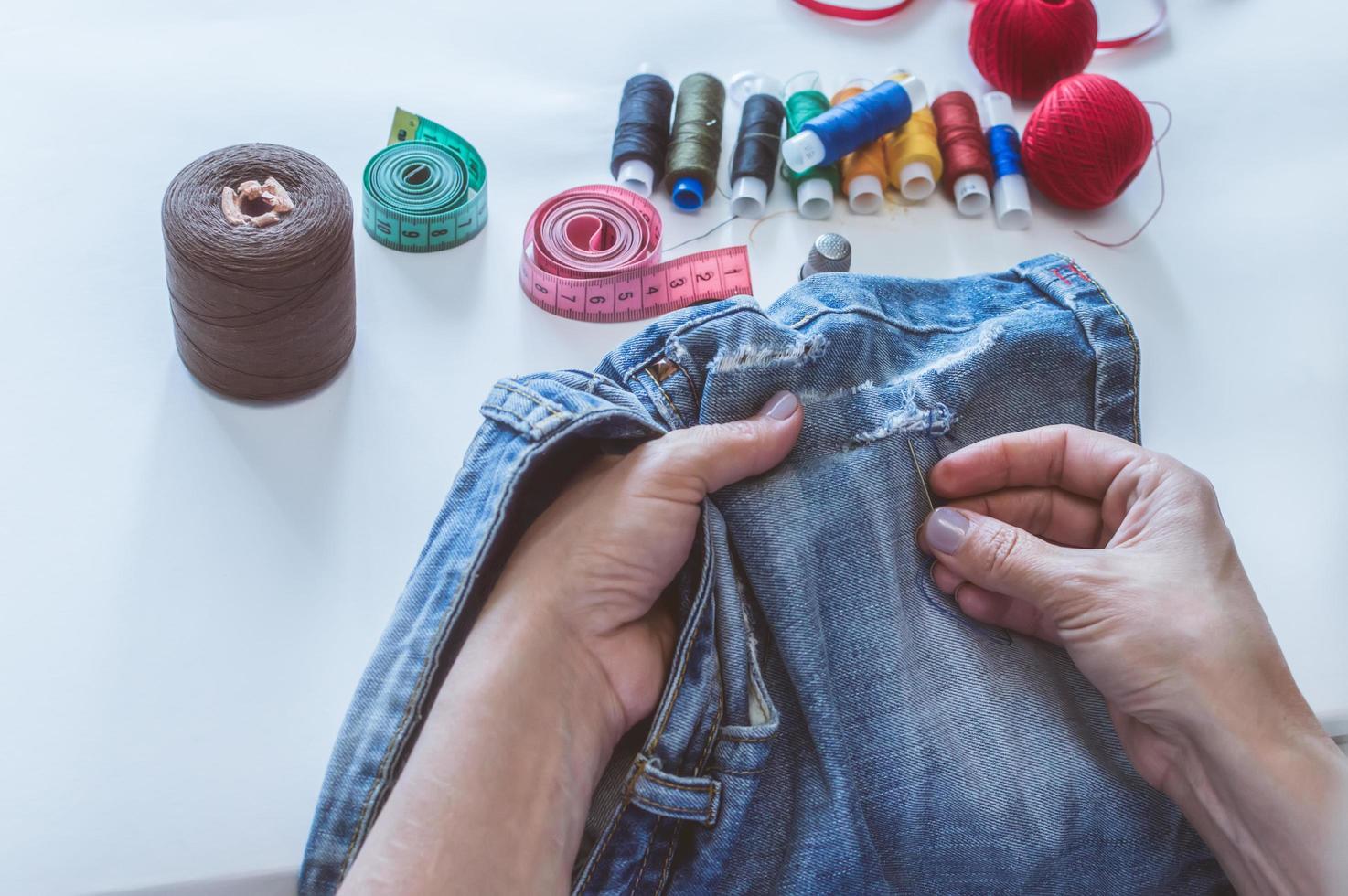 women's hands, a tailor sews clothes at a table on which spools of thread lie photo