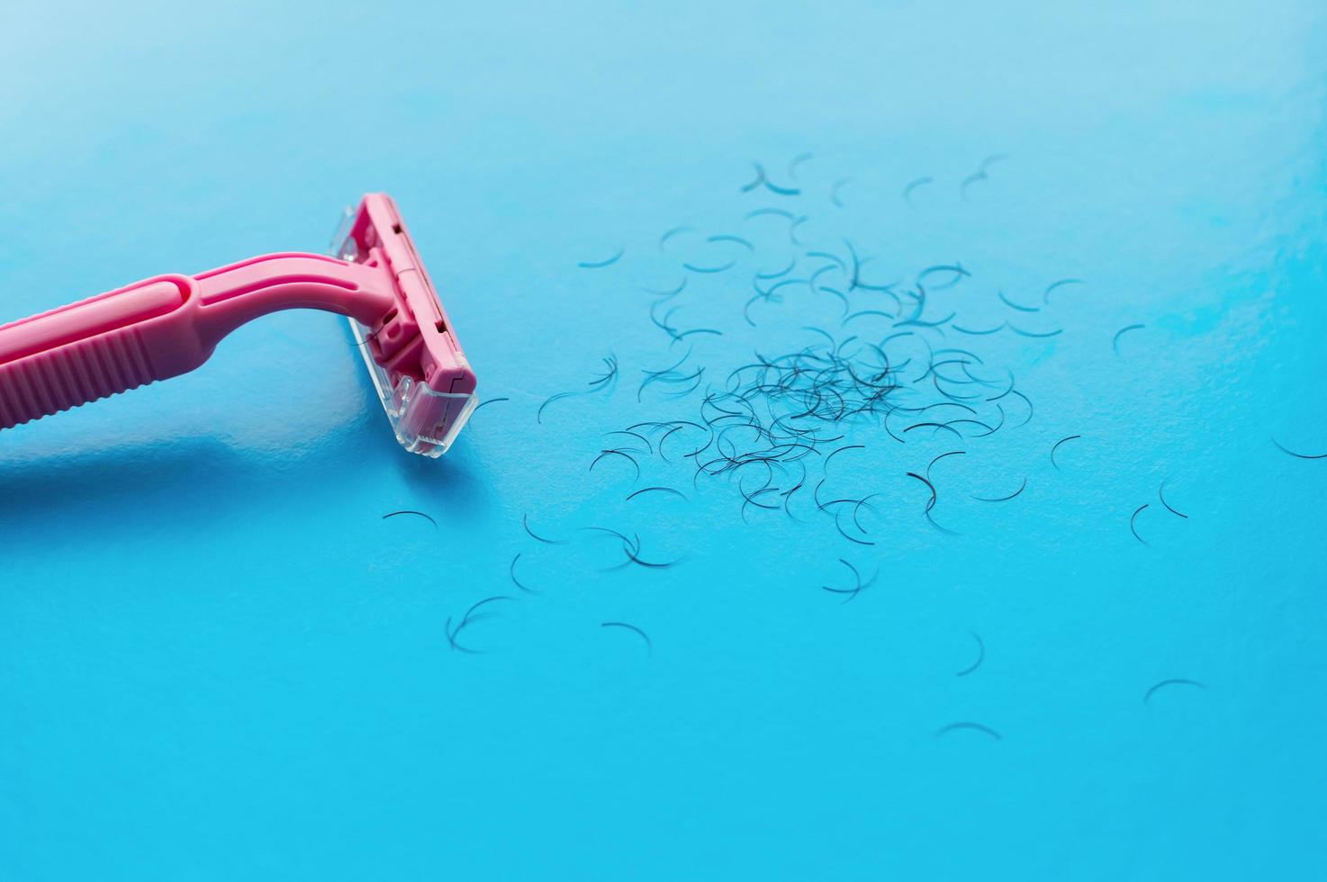 Máquina de afeitar para mujer rosa y cabello sobre un fondo azul. el concepto de afeitado femenino. foto