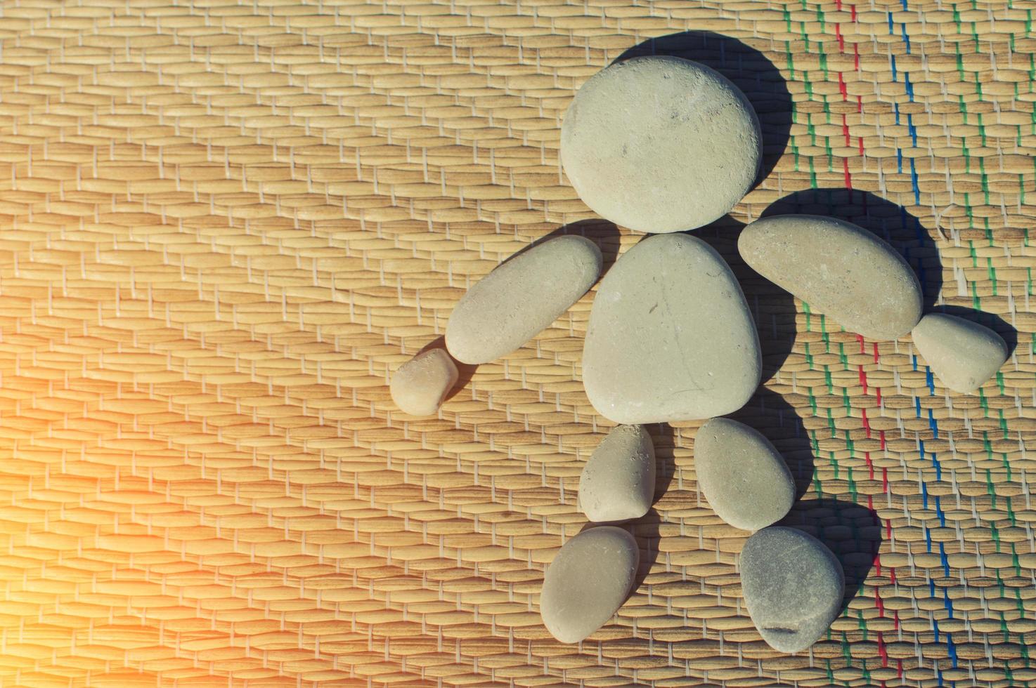 A figure of a little man made of sea pebbles on a straw blanket. Cute children's games on the beach. The concept of tourism and beach holidays. photo