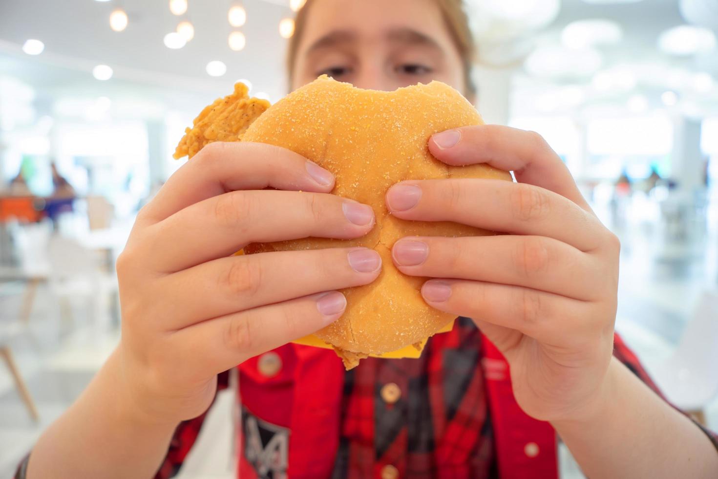 Adolescente hambrienta comiendo una hamburguesa con queso en el patio de comidas del centro comercial. comida chatarra. foto