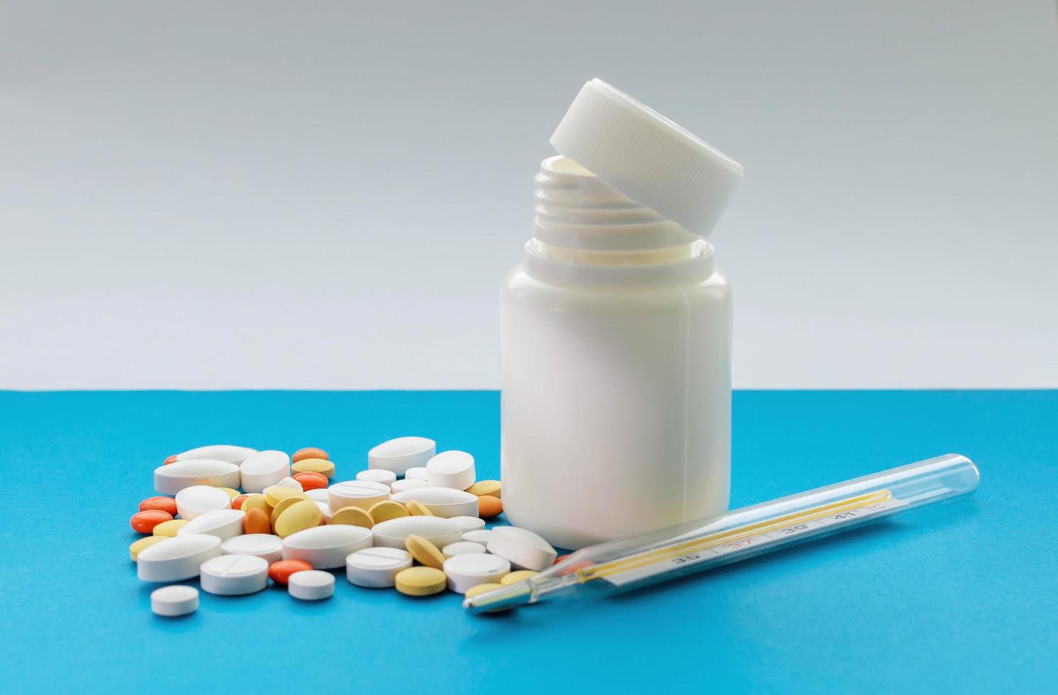 A jar of pills and a thermometer on a blue background. Concept of health protection. photo